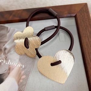 Detailed macro view of brushed gold metal flower and heart charms on high-stretch hair ties