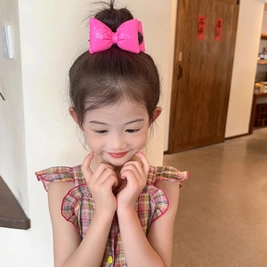 Detail of a bright pink bow hair clip for girls worn on a bun hairstyle in a home setting