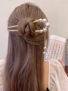 Detailed view of a gold U-shaped hair pin with pearls and delicate tassel in a bun hair