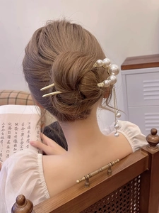 Detail showing an elegant gold U-shaped hairpin with pearl tassels in a bun hairstyle