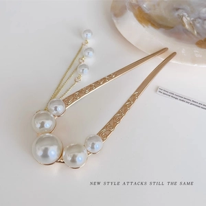 Detail view of a gold U-shaped hair pin with elegant white pearls and a delicate tassel