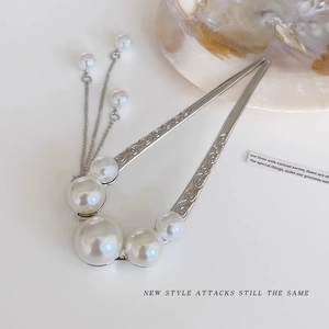 Macro detail of silver U-shaped hair pin with pearls and tassel on white background
