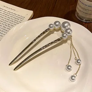 Elegant gold U-shaped hair pin with white pearls and long tassel on a white plate