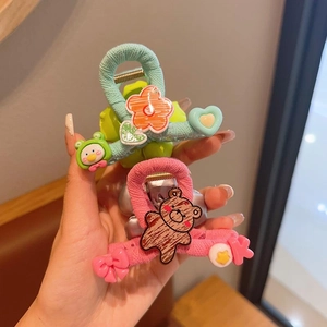 Close-up of cute cartoon hair claws with woven fabric and 3D floral bear details