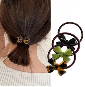 Three bow-knot hair ties in black, dark green and tortoiseshell on a neutral background