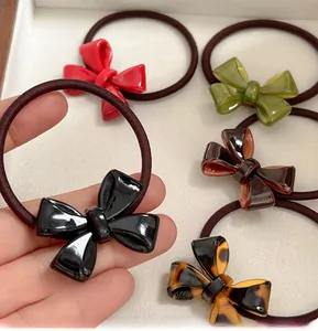 Close-up of five colorful high-gloss acrylic bow hair ties on a cream velvet display stand