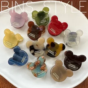 Detailed overhead view of twelve colorful acetate bear-shaped hair claws on a ceramic plate