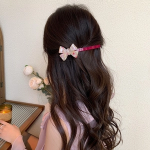 Close-up of a pink resin bow hair clip with floral patterns worn on a model back hair