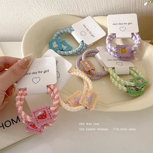 Handwoven elastic hair ties with colorful cartoon charms displayed in a ceramic tray