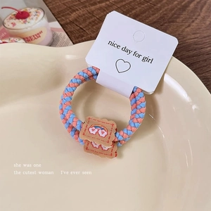 Detail of hand-woven hair tie with rainbow biscuit embroidery on a ceramic tray