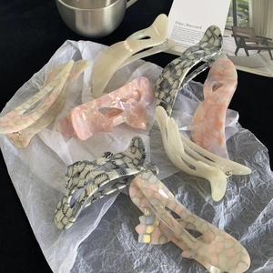 Iridescent acetate hair clips in various marble patterns shown on a decorative background