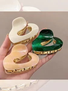 Close-up of three acetate heart-shaped hair claws in marble green, cream and pearl pink