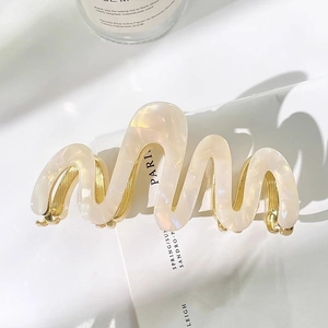 Détail d'une pince à cheveux en acétate crème avec ressort doré et texture marbrée