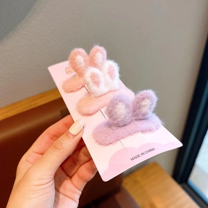 Detailed view of three plush rabbit ear hair clips in pink, white and purple on card