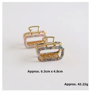 Detail view of square marble acetate hair claws with gold springs measuring 6.3cm by 4.8cm