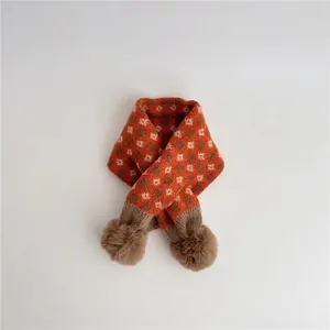 Detail of baby winter scarf featuring vintage orange plaid knit pattern and pompom decor