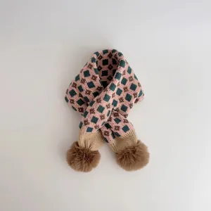 Close-up of pink and green checkered knit scarf with two brown faux fur pom poms
