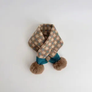 Detailed knit pattern of brown checkerboard baby scarf with soft pompom charms