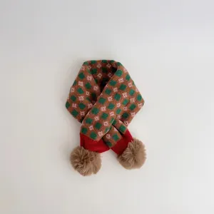 Detail view of retro red and green checkered knit scarf with soft faux fur pom-poms