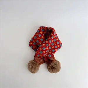 Close-up of knit geometric jacquard scarf with red argyle pattern and brown pom-poms