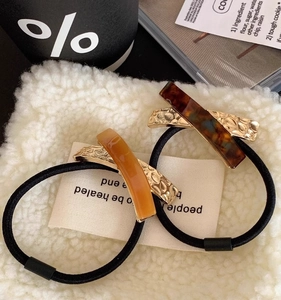 Detailed close-up of acetate and metal hair ties on soft white textured fabric
