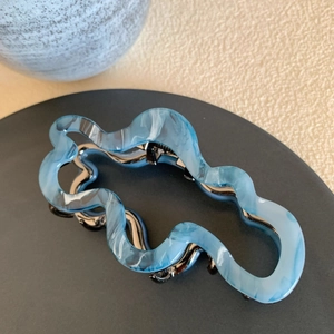 Detailed macro view of large wavy blue and white acetate hair claw clip with metal spring