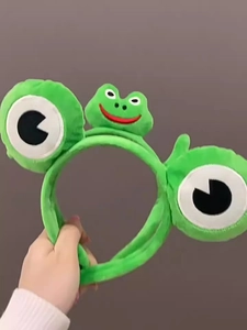 Détail d'un bandeau en peluche grenouille verte avec yeux 3D et décoration souriante