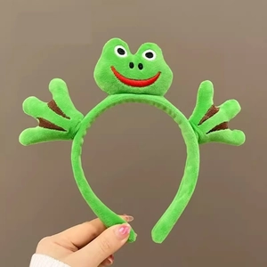 Détail du serre-tête grenouille en peluche verte avec de grands yeux et de jolies pattes