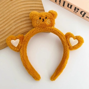 Dettaglio di un cerchietto di peluche giallo con orsetto ricamato e orecchie con cuori