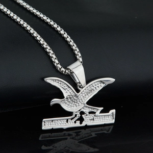 Detailed shot of silver stainless steel eagle pendant with box chain on black texture
