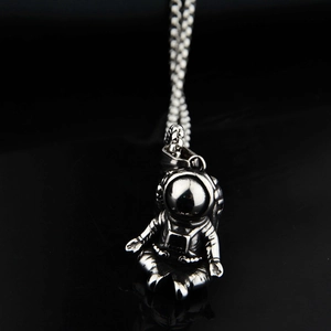 Macro shot of silver astronaut pendant with bead chain on a black reflective background