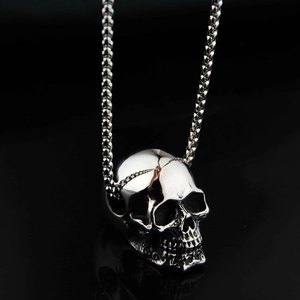 Macro close-up of polished steel skull pendant on box chain over black reflection