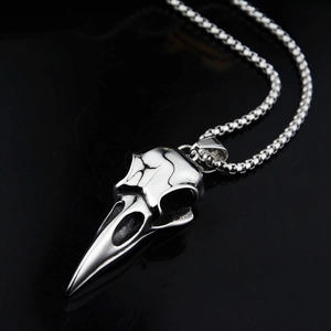 Pendentif crâne de corbeau en acier poli avec chaîne à billes sur surface noire brillante