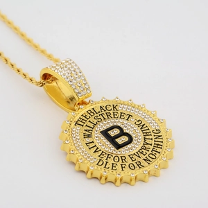 Detail of gold hip hop bottle cap pendant with white crystals and B logo on rope chain