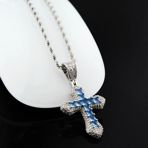 Détail du collier croix hip hop argenté avec pierres de zircon bleues et chaîne torsadée fine