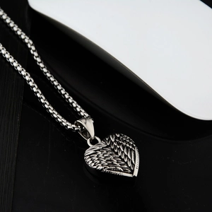 Vue macro du pendentif cœur ailé en acier inoxydable argenté avec détails de plumes