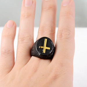 Detail of matte black signet ring with golden inverted cross and diamond texture
