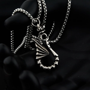 Macro shot of silver dragon wing pendant with textured details on steel box chain