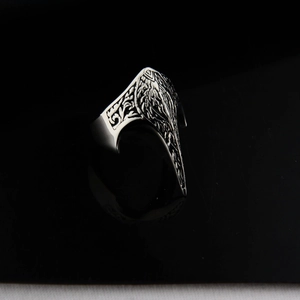 Macro detail of gothic eagle beak ring with floral carvings on polished black surface