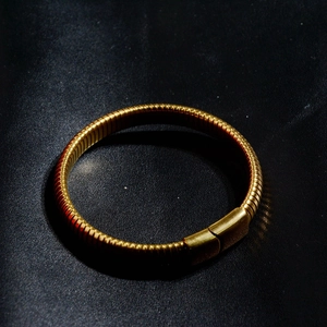 Detailed close-up of golden titanium steel bracelet with spiral texture and rectangular clasp