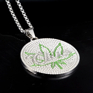 Détail macro du collier médaillon serti de strass avec motif de feuille verte sur fond noir