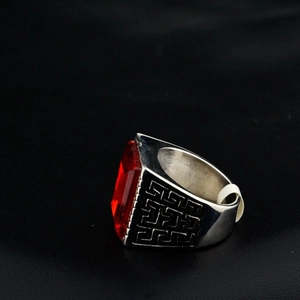 Macro view of men's silver steel ring featuring a red square gemstone and Greek meander engraving
