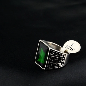 Detail of square green gemstone on men's steel ring with silver Greek key pattern