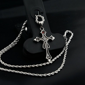 Détail macro du collier croix gothique avec pierre rouge et chaîne torsadée argent