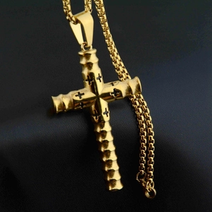 Detail eines goldenen Zylinderkreuz-Anhängers mit Schnitzereien an einer Perlen-Boxkette