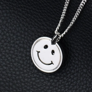 Gros plan d'un pendentif rond visage souriant argenté avec chaîne fine sur cuir noir
