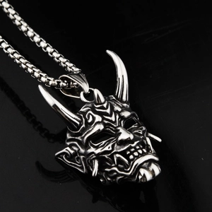 Gros plan d'un pendentif masque Hannya argenté sur chaîne box avec fond miroir noir