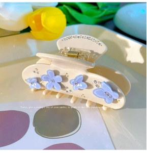 Dettaglio di un fermaglio per capelli crema con fiori viola, farfalla e strass luccicanti