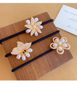 Detail of three pearl floral hair ties on a wooden stand with elegant gold finish accents