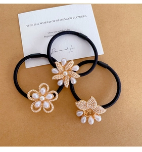Close-up of three black hair ties with elegant white pearl flower charms on a rustic background